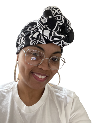 A smiling person wears a black and white patterned head wrap, large hoop earrings, and glasses against a black background.