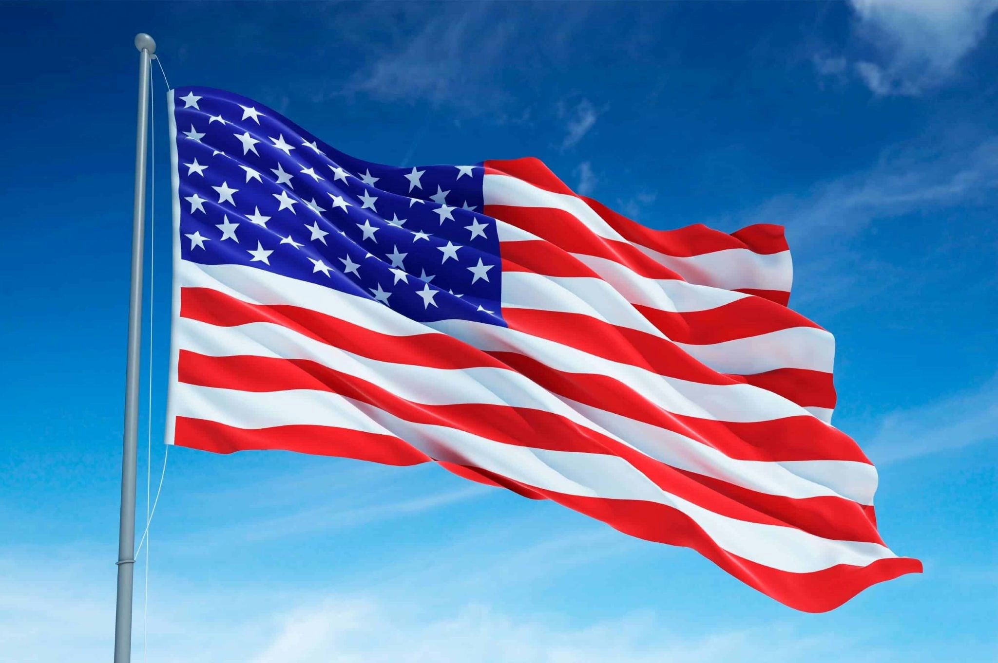 The American flag waves proudly against a clear blue sky with wispy clouds.