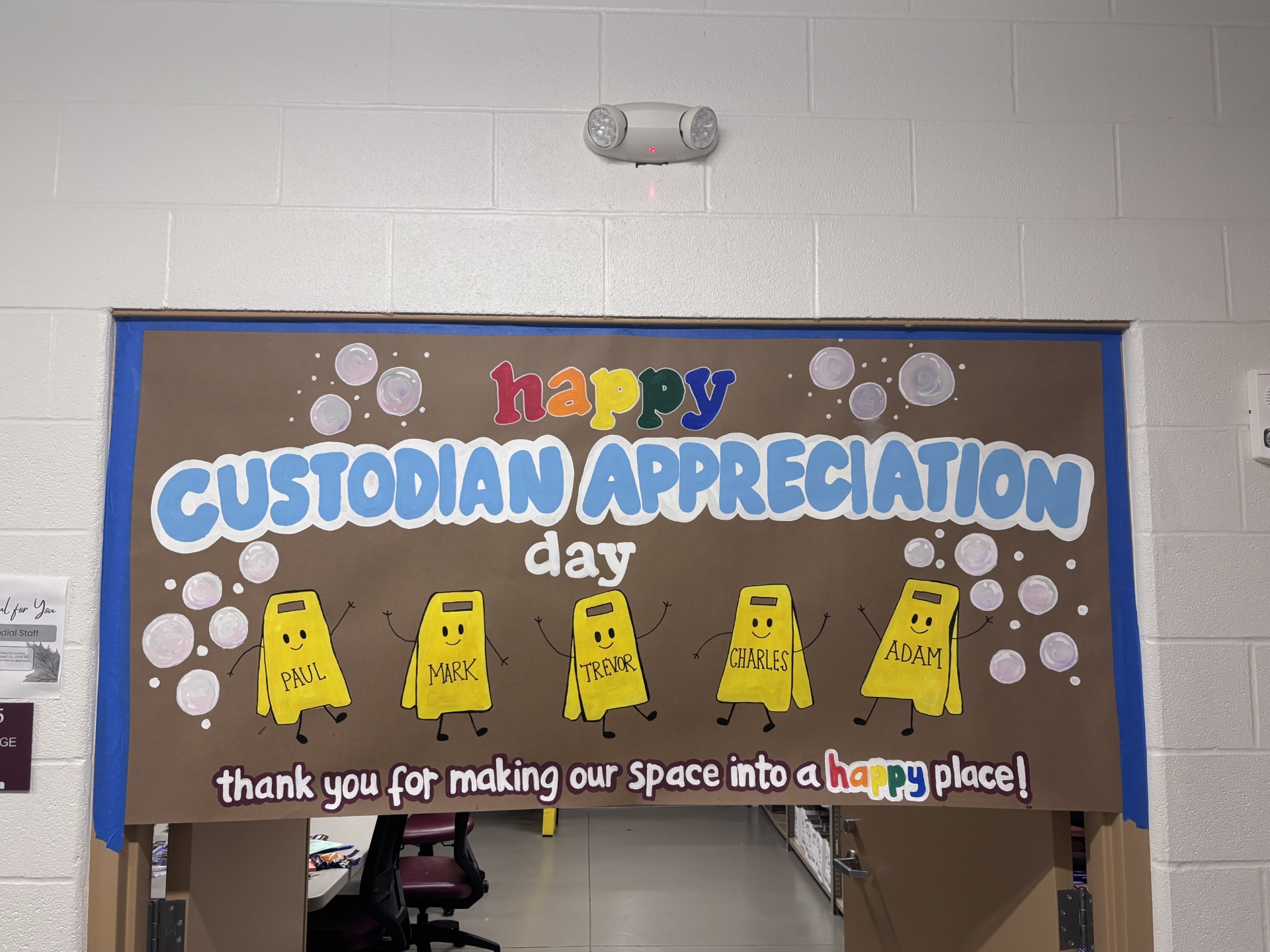 A school bulletin board reads "Happy Custodian Appreciation Day" with drawings of yellow wet floor signs labeled Paul, Mark, Trevor, Charles, and Adam.