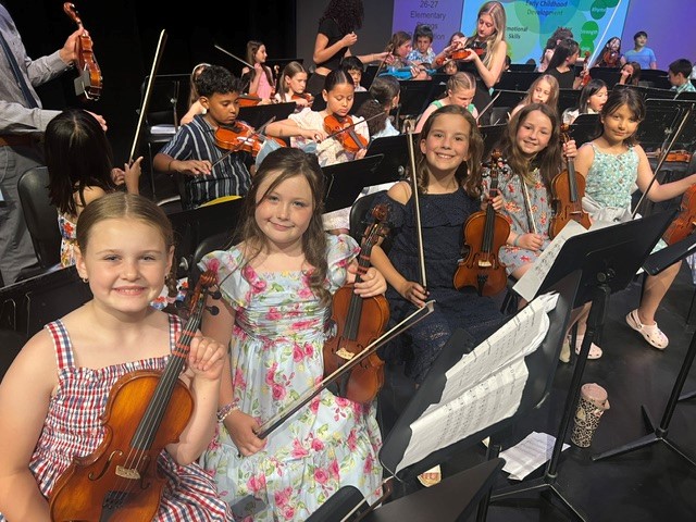 Young musicians in formal attire hold violins, ready to perform in an orchestra.