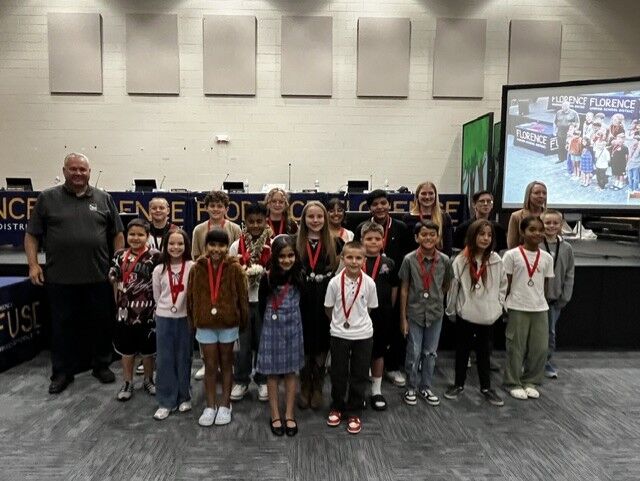A group of children and adults pose together on a stage, proudly wearing medals around their necks.