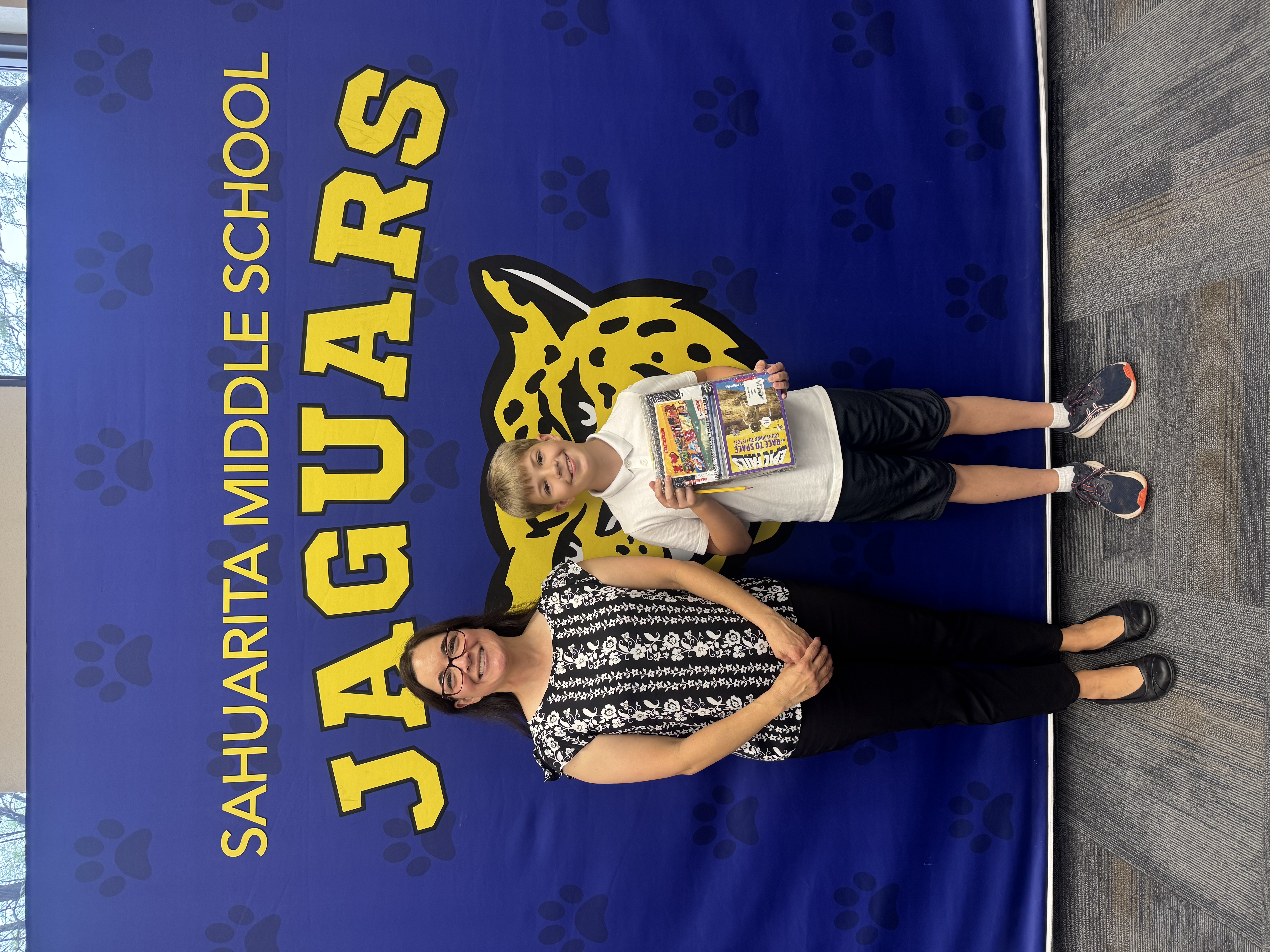 A teacher and a student stand in front of a blue banner.