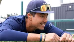 Jayce in a navy uniform and cap lies on the grass, smiling with hearing aid in his ear.