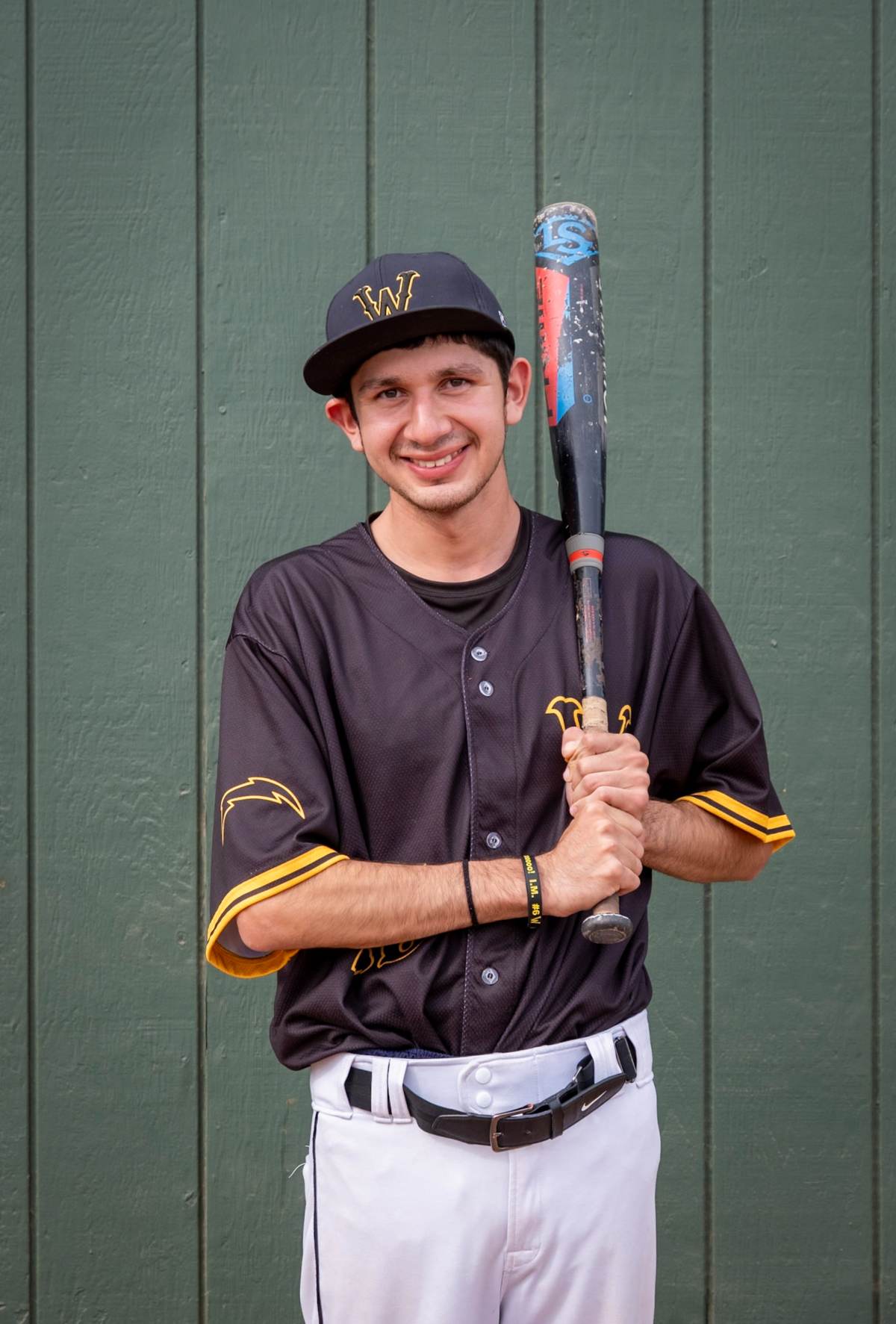 kevin in a baseball uniform smiles, holding a bat.