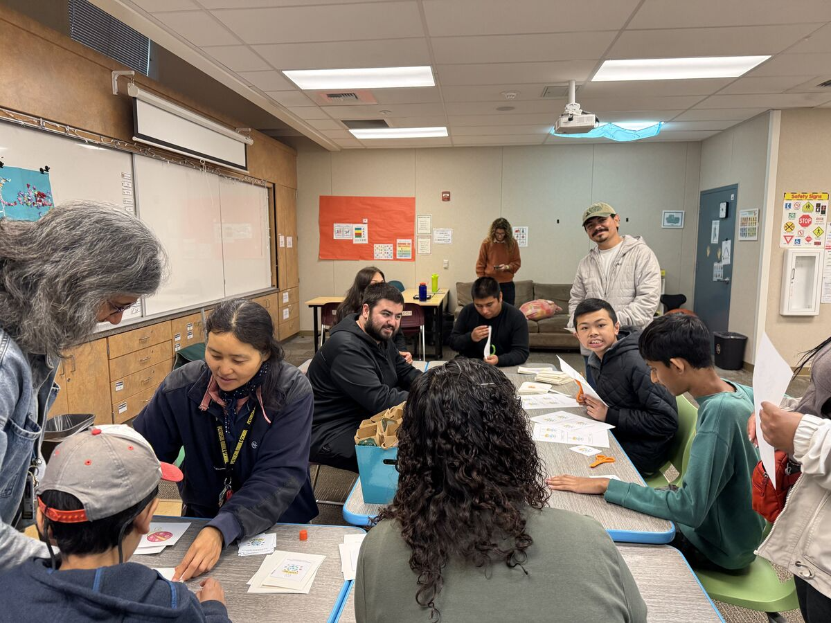 Students and adults collaborate on a craft project at tables in a classroom.