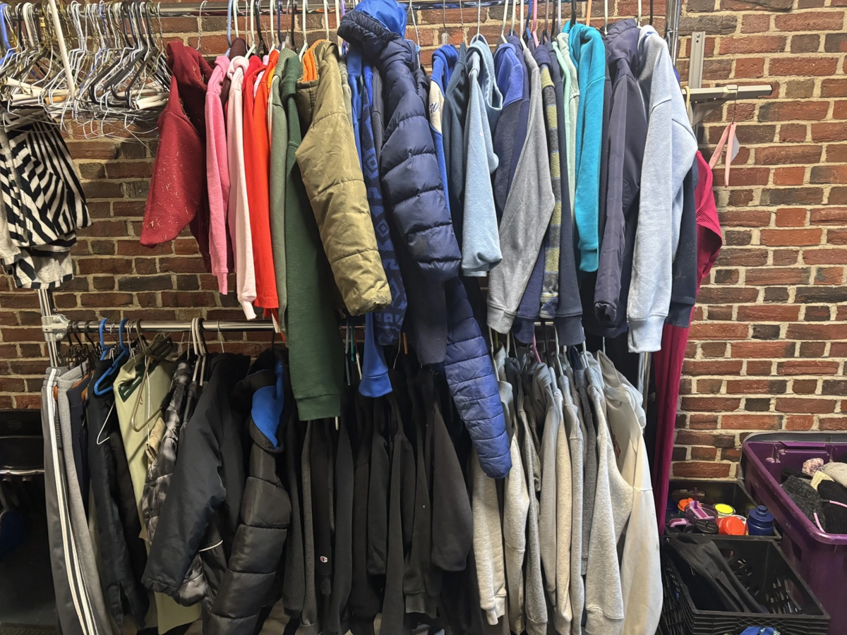 A rack of colorful jackets and hoodies hangs against a brick wall.