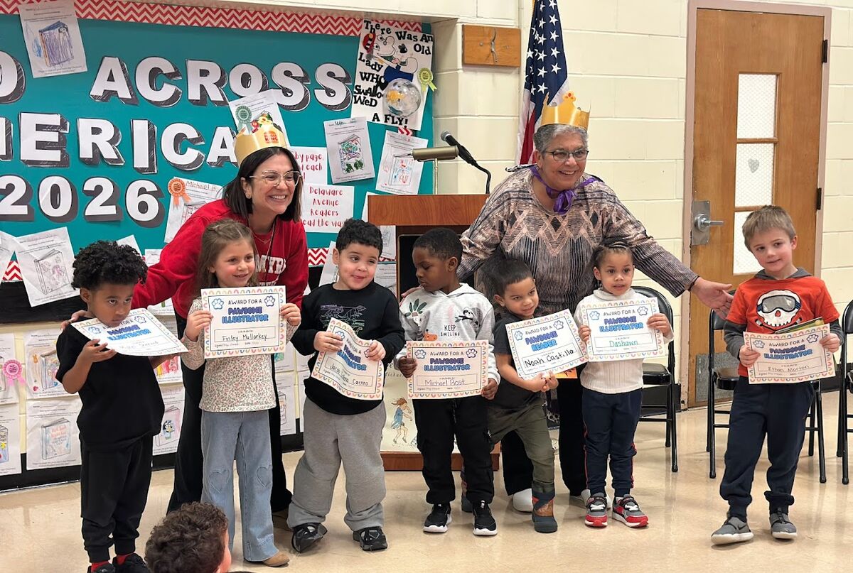 Children and adults in a classroom setting, with children holding awards for 'Pawsome Illustrator' and 'Pawsome Reader'.