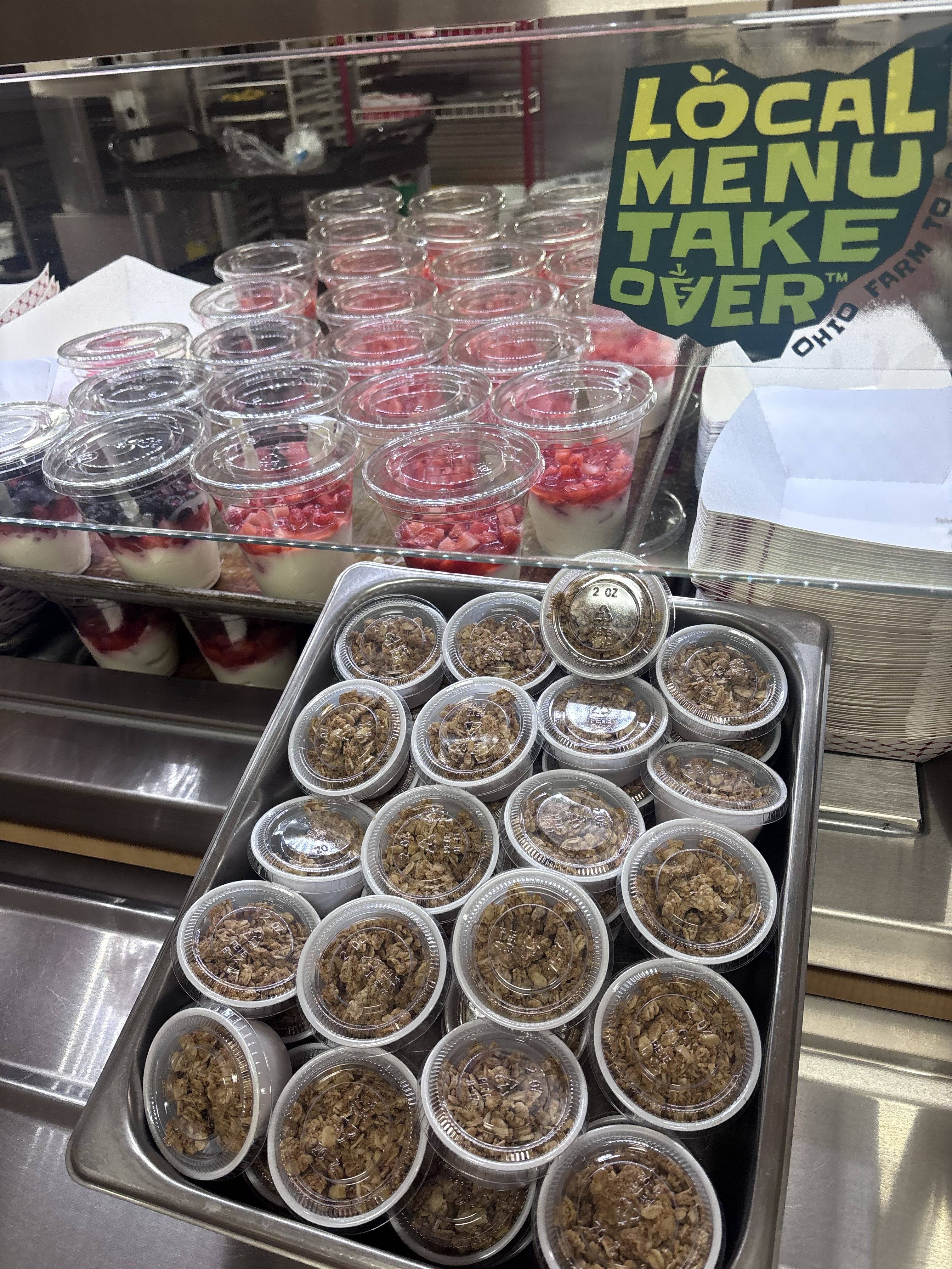 A metal tray holds numerous small cups of granola beneath a glass display case.