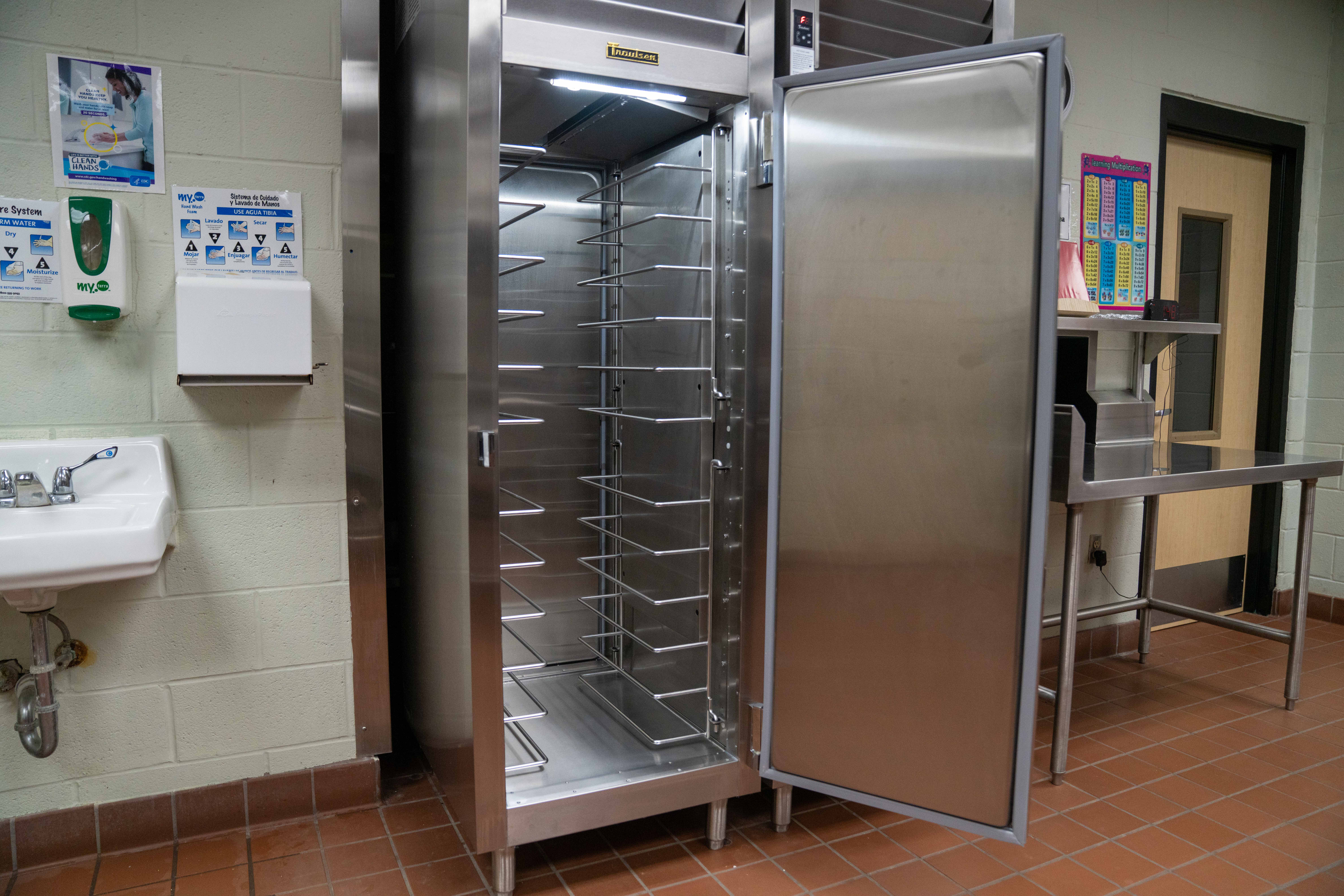 An empty, stainless steel commercial oven with multiple racks is open in a kitchen.