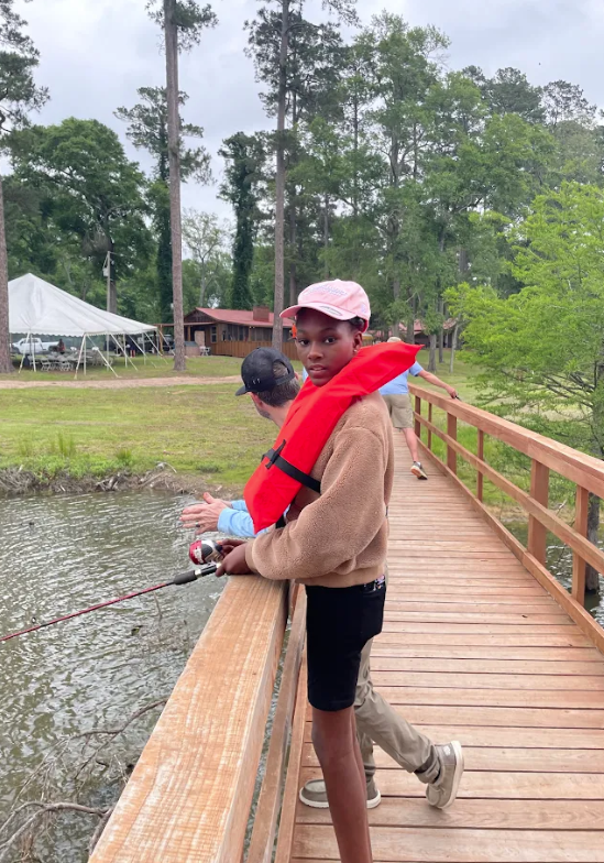 A young person in a life vest fishes from a wooden pier with an adult.