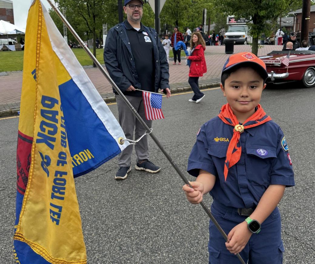 A young Boy Scout holds a flag pole with a large banner and a small American flag.