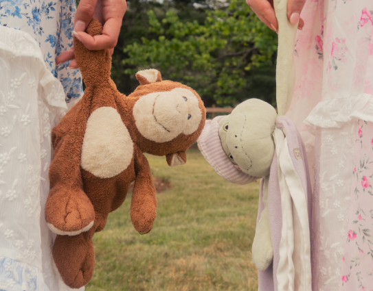 Two people hold up plush stuffed animals, a brown monkey and a light green turtle, outdoors.