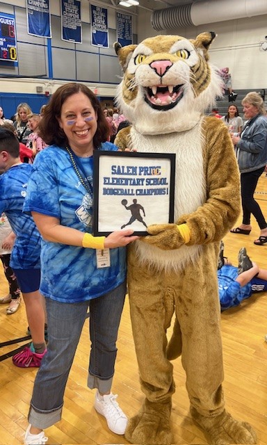 A woman and a tiger mascot hold a framed award for "Salem Pride Elementary School Dodgeball Champions".