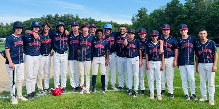 A baseball team of young men in navy and red uniforms stand together on a grassy field.