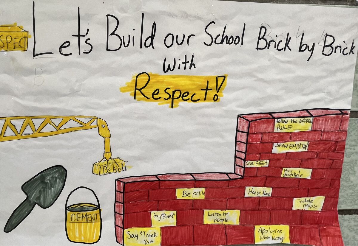 A hand-drawn school poster reads, 'Let's Build our School Brick by Brick With Respect!'.