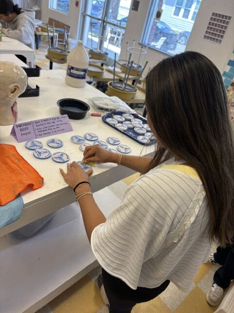 A young person is arranging small circular objects with blue emblems on a white table.