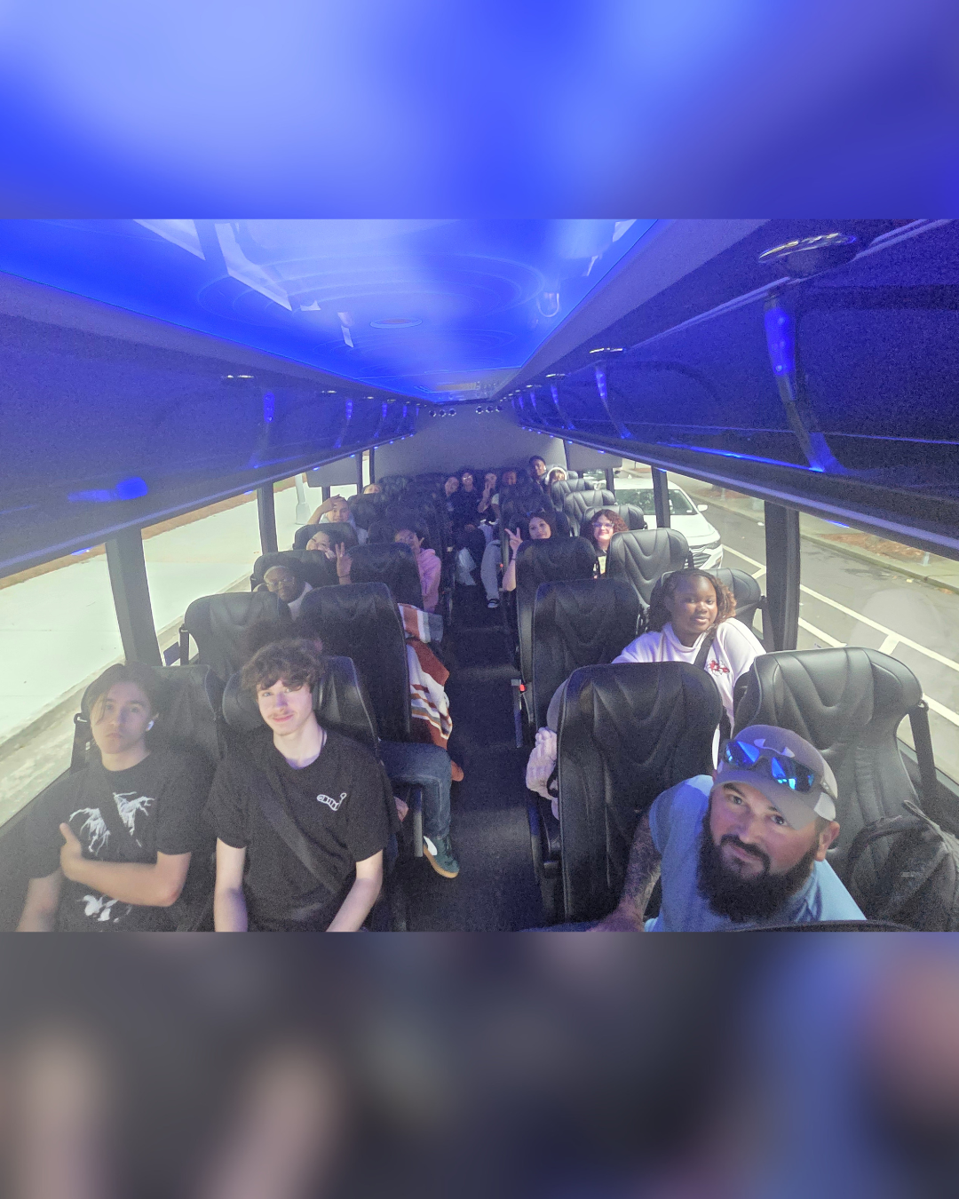 A group of people, mostly young adults, are seated on a bus with blue interior lighting.