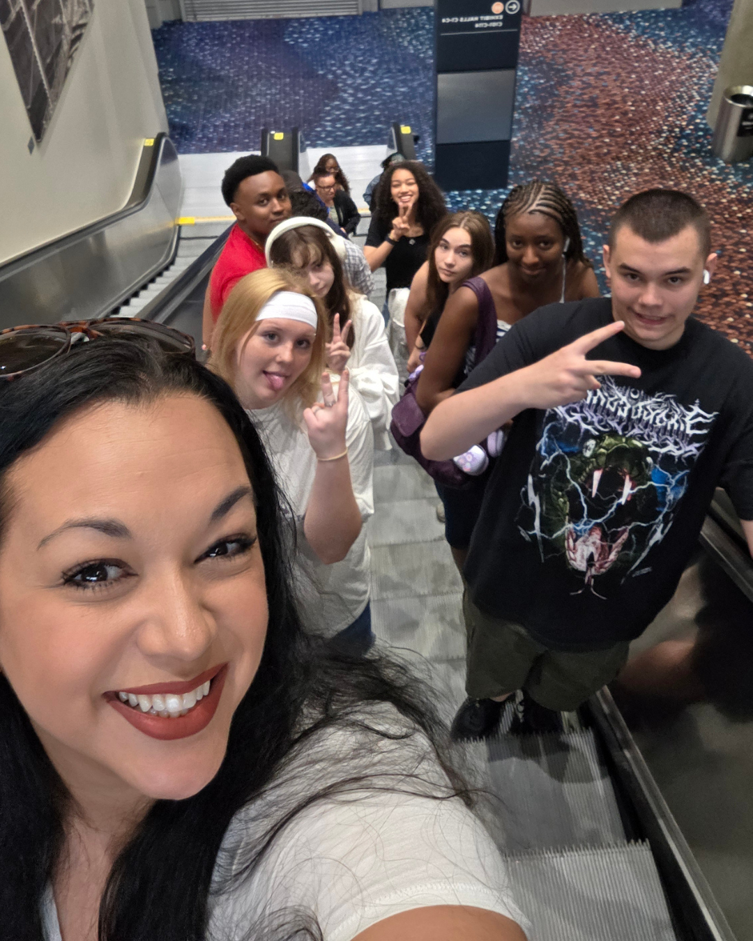 A group of young people and an adult smile while riding an escalator.