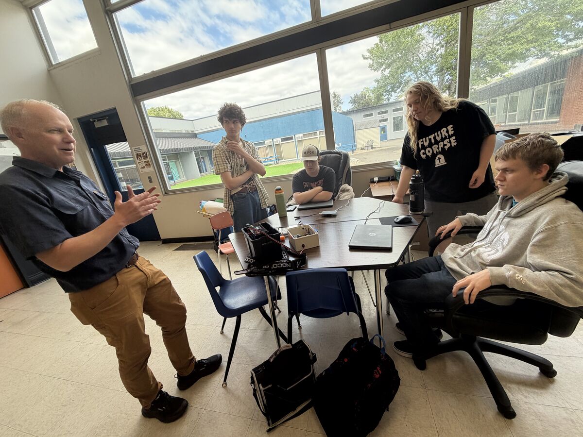 4 students around a table looking at a machine while a teacher looks on