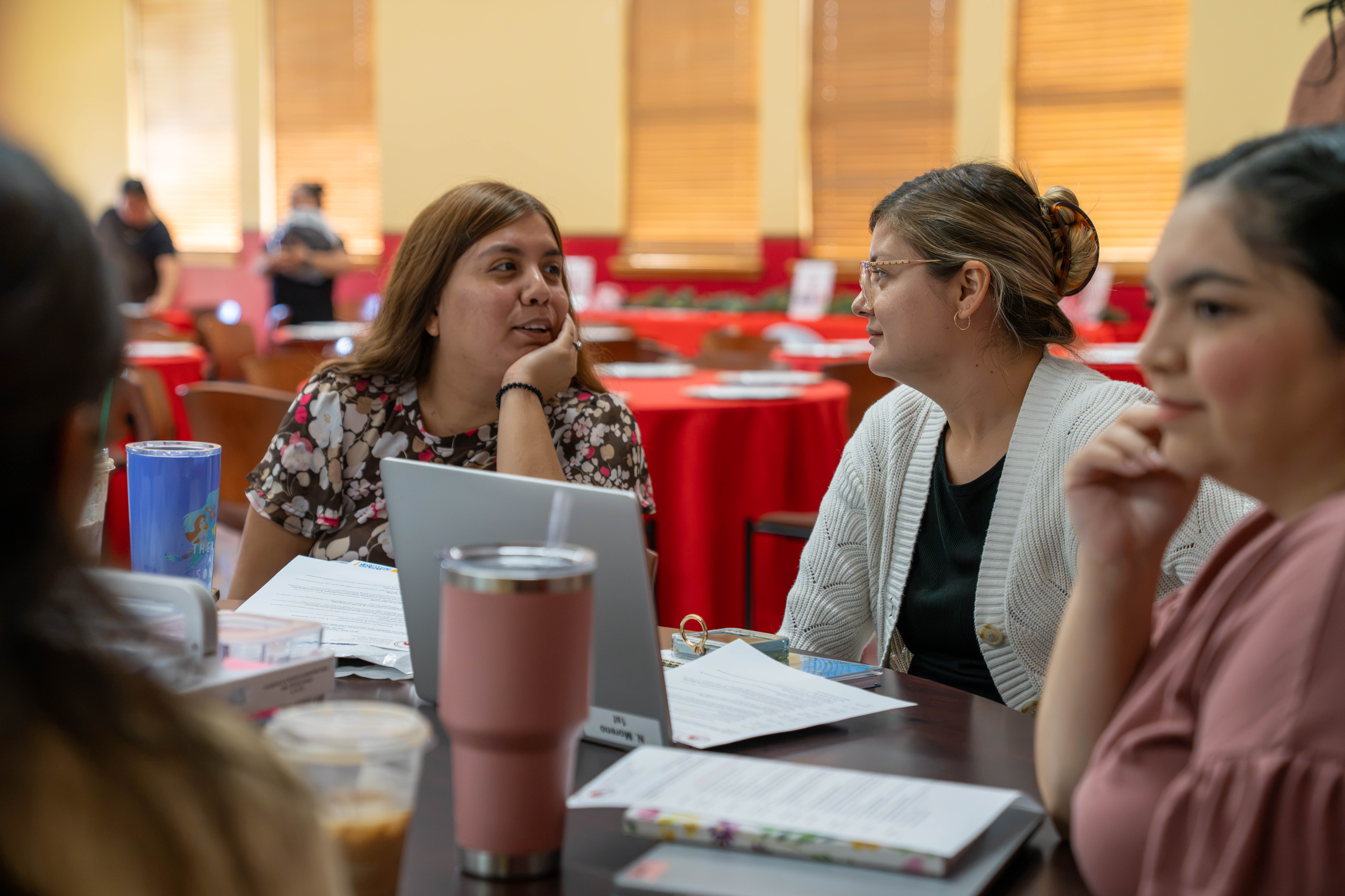 Three women are seated at a table, engaged in conversation during a meeting.