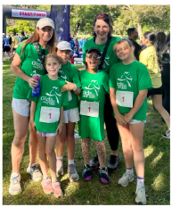 Two adults and four young girls in green t-shirts pose for a photo at a race event.
