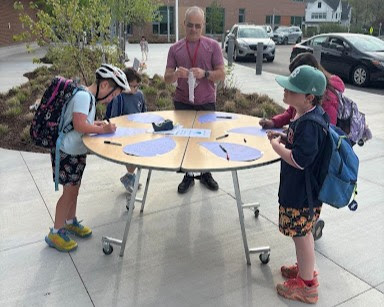 Mr. Guzzi standing outside in front of table as students sign their name for walking and rolling to school. 