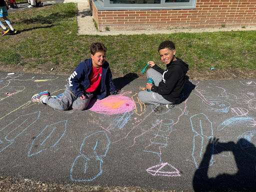 First and third grade buddies draw with chalk outside. 