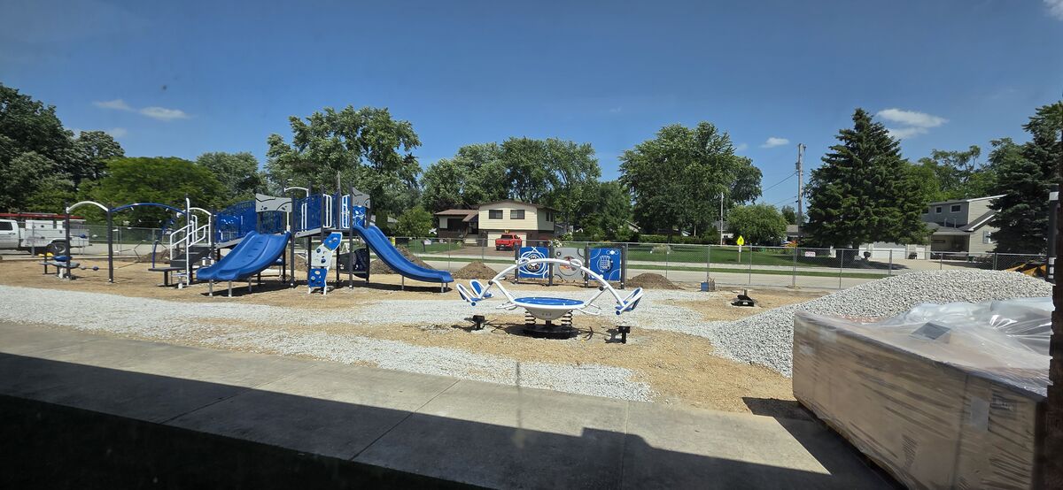 A new blue and white playground with slides and a merry-go-round is under construction.
