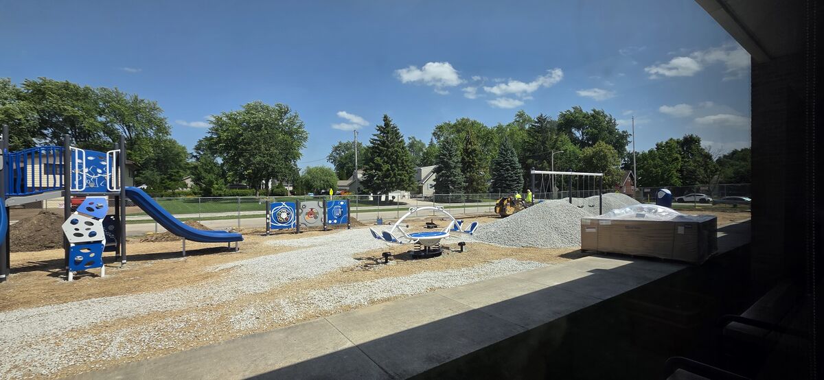 A new playground is under construction with blue and white equipment, gravel, and a small bulldozer.