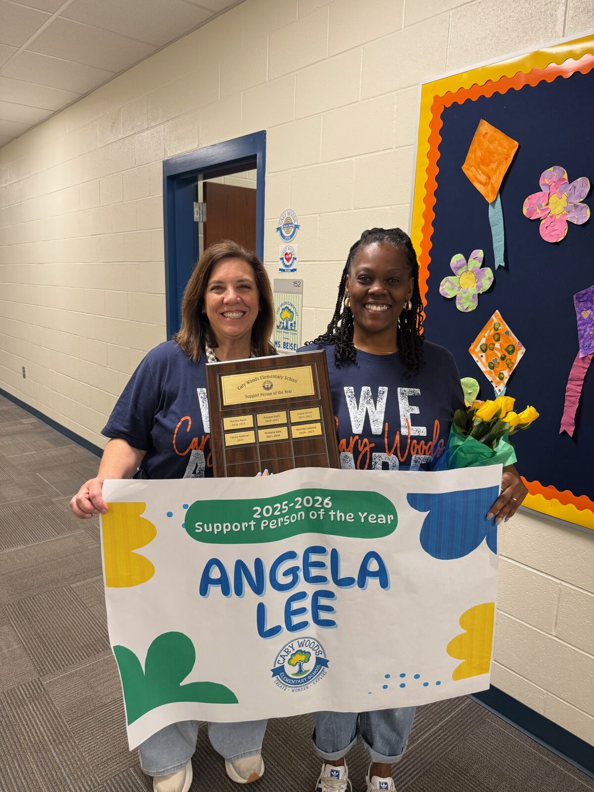 Two women smile as they hold a "Support Person of the Year" award and banner for Angela Lee at Cary Woods Elementary School.