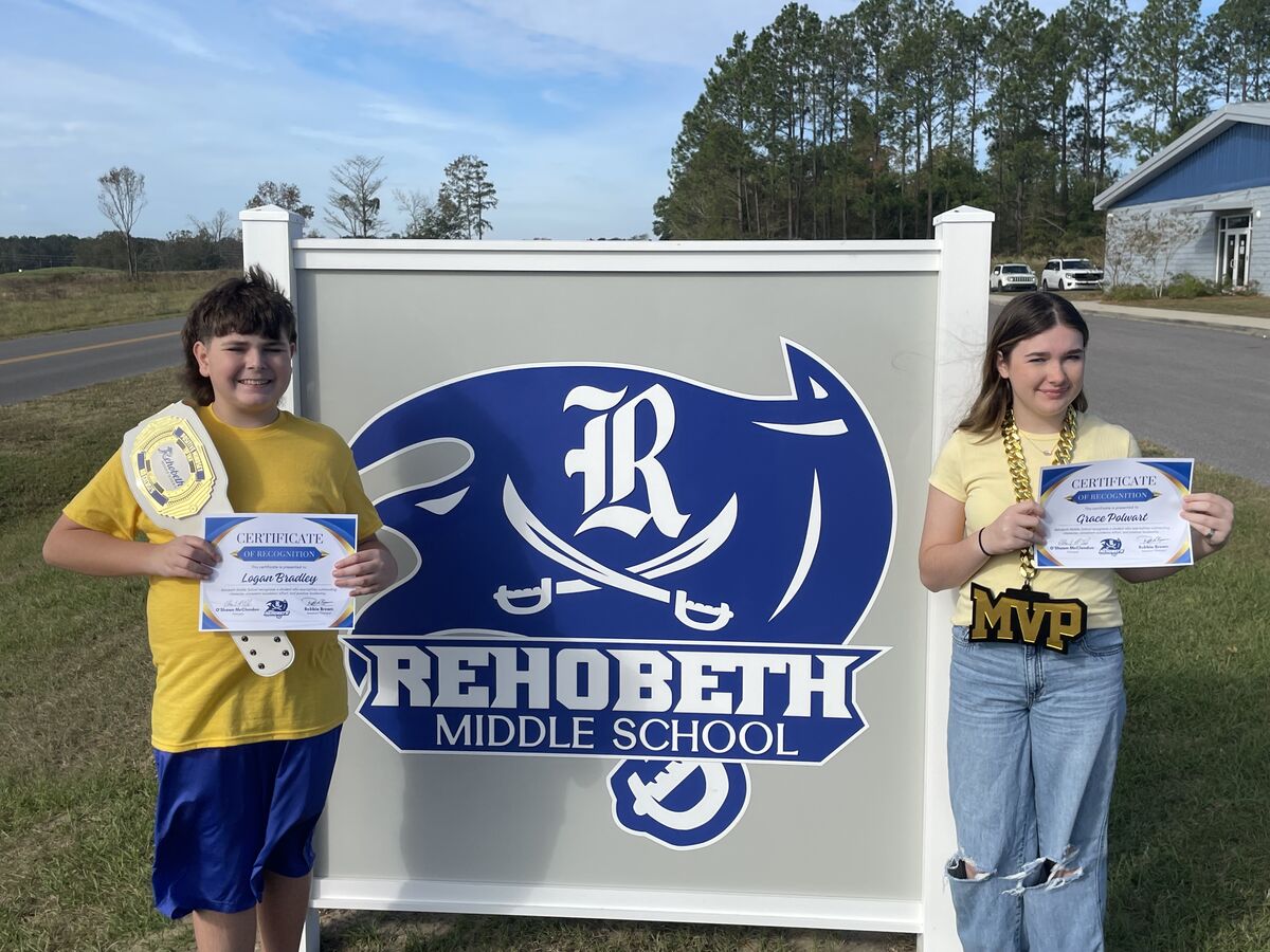 Two students proudly hold certificates of recognition in front of a large Rehoboth Middle School sign.