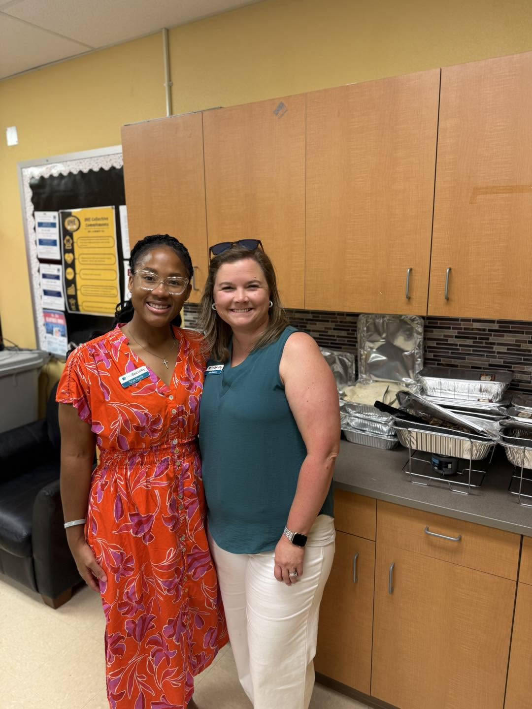 Two women stand together in front of a counter with catering trays.