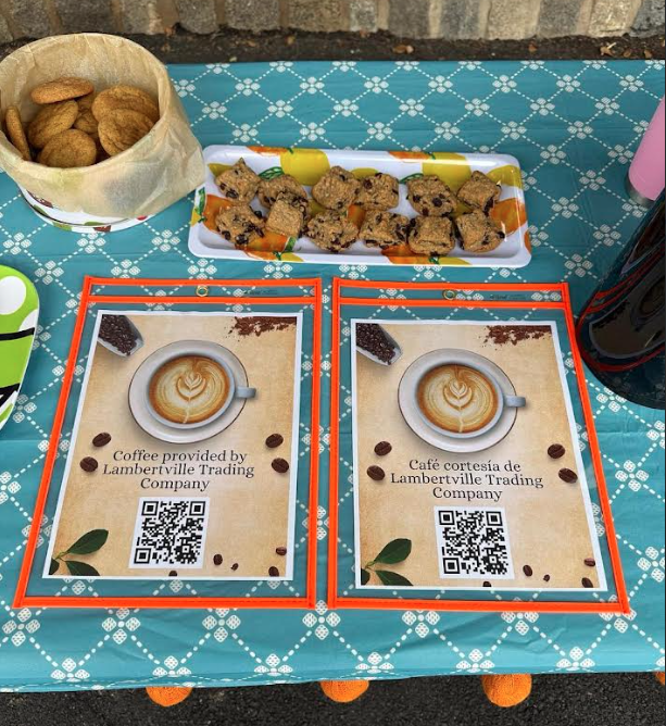 A table covered in a teal patterned tablecloth displays a container of cookies, a tray of baked squares, and two signs advertising coffee by Lambertville Trading Company.