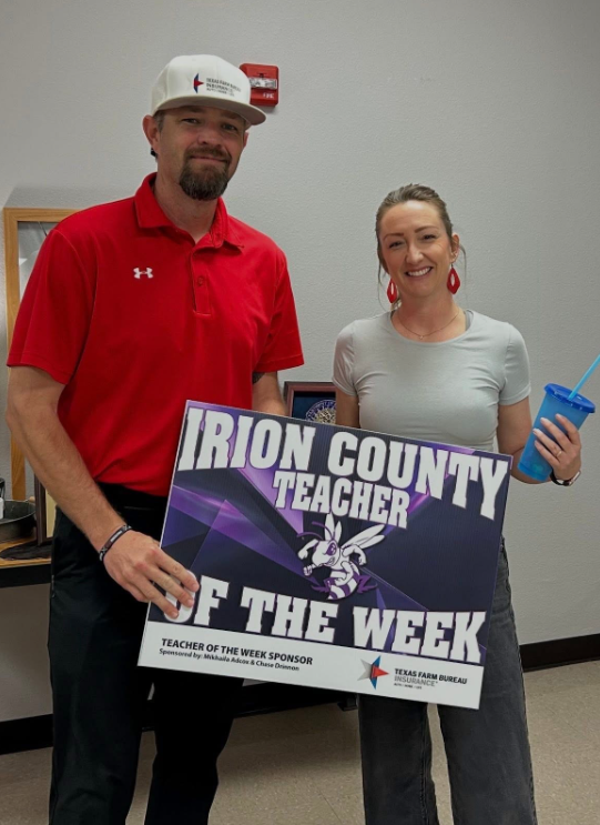 A man in a red shirt and a woman in a grey shirt hold a sign that reads "IRION COUNTY TEACHER OF THE WEEK".