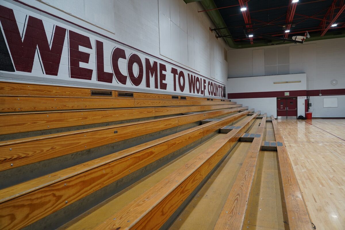 Empty wooden bleachers in a gymnasium with "WELCOME TO WOLF COUNTRY" painted on the wall.