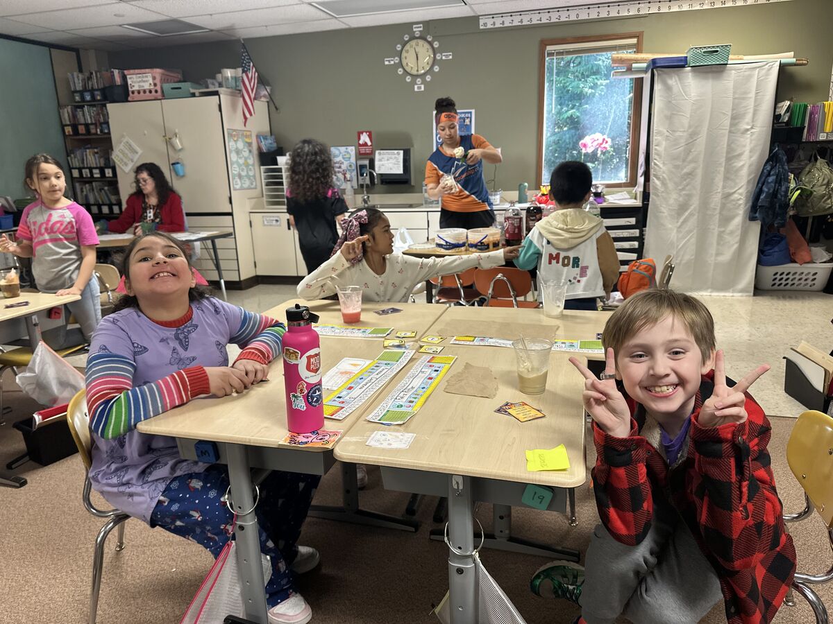 Children sit at desks in a classroom, some smiling and making peace signs.