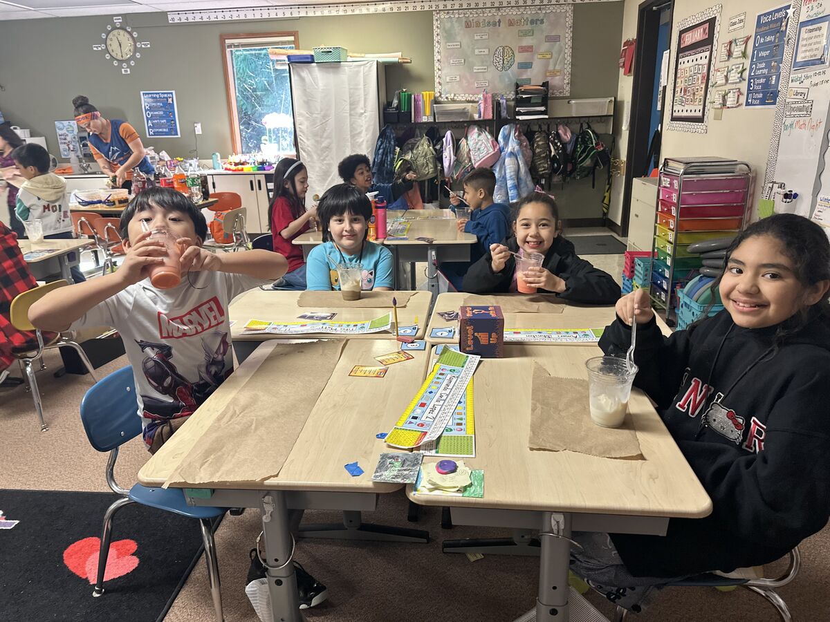 Children in a classroom enjoy drinks and snacks at their desks.