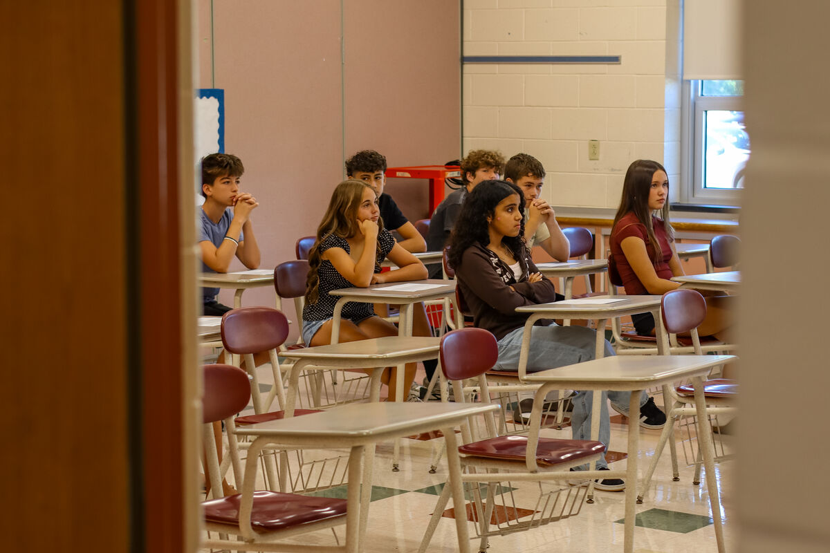 Students sit at desks in a classroom, attentively listening.