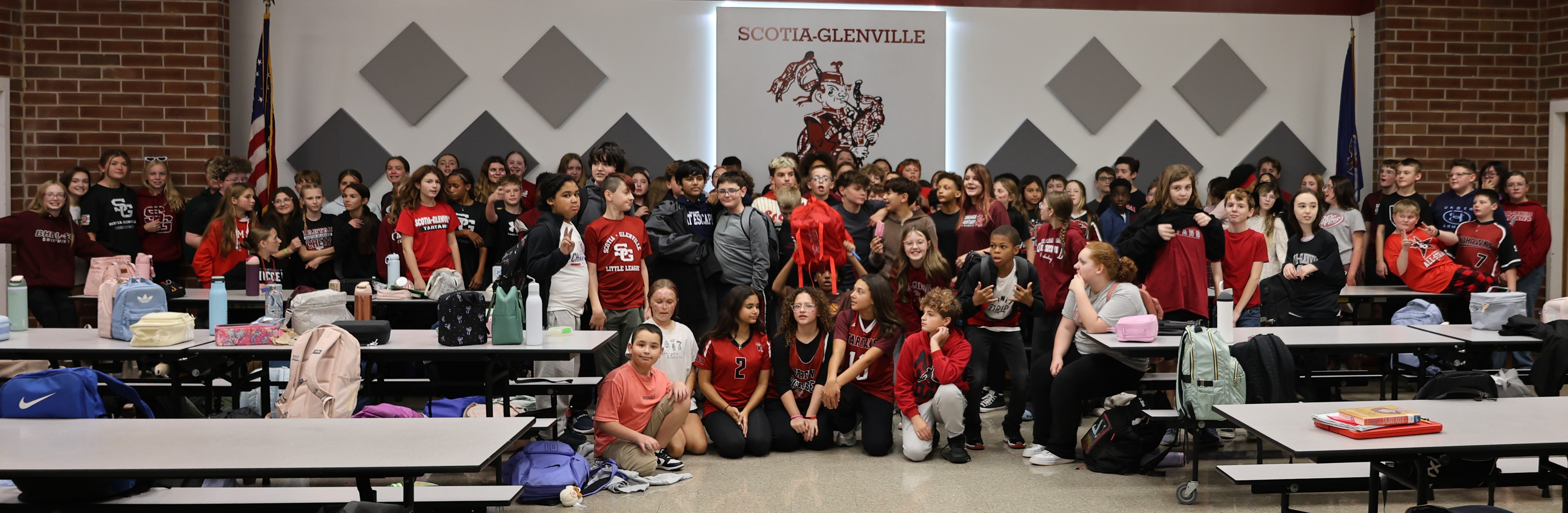7th grade class gathers in a school cafeteria for a group photo, with the Scotia-Glenville sign visible on the back wall.