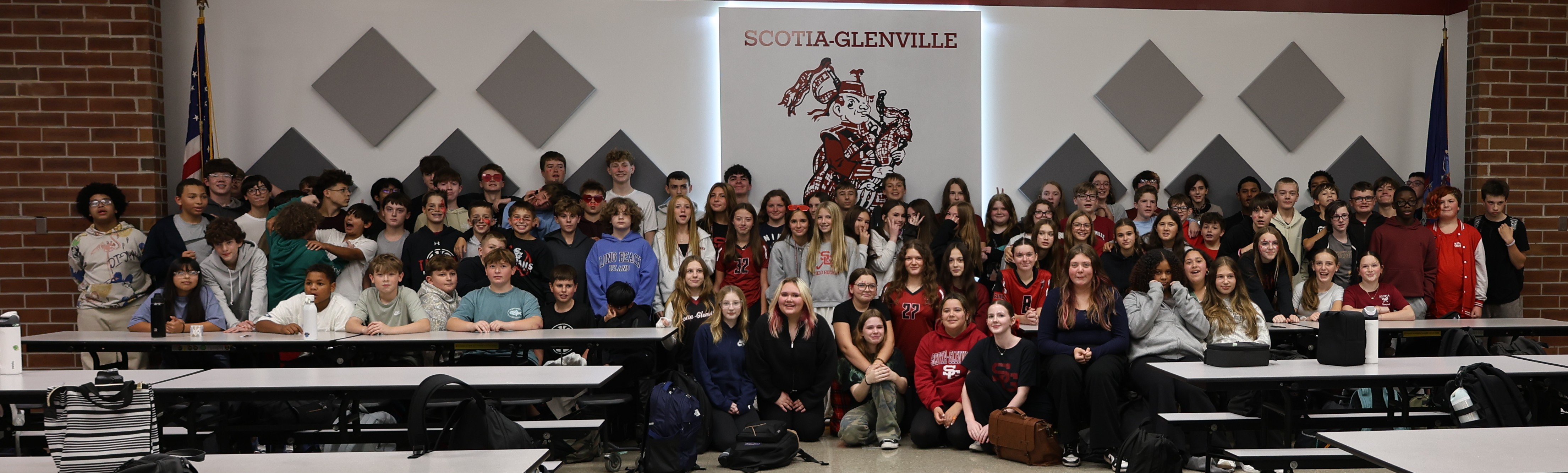 8th grade class gather indoors for a group photo in front of a Scotia-Glenville sign.