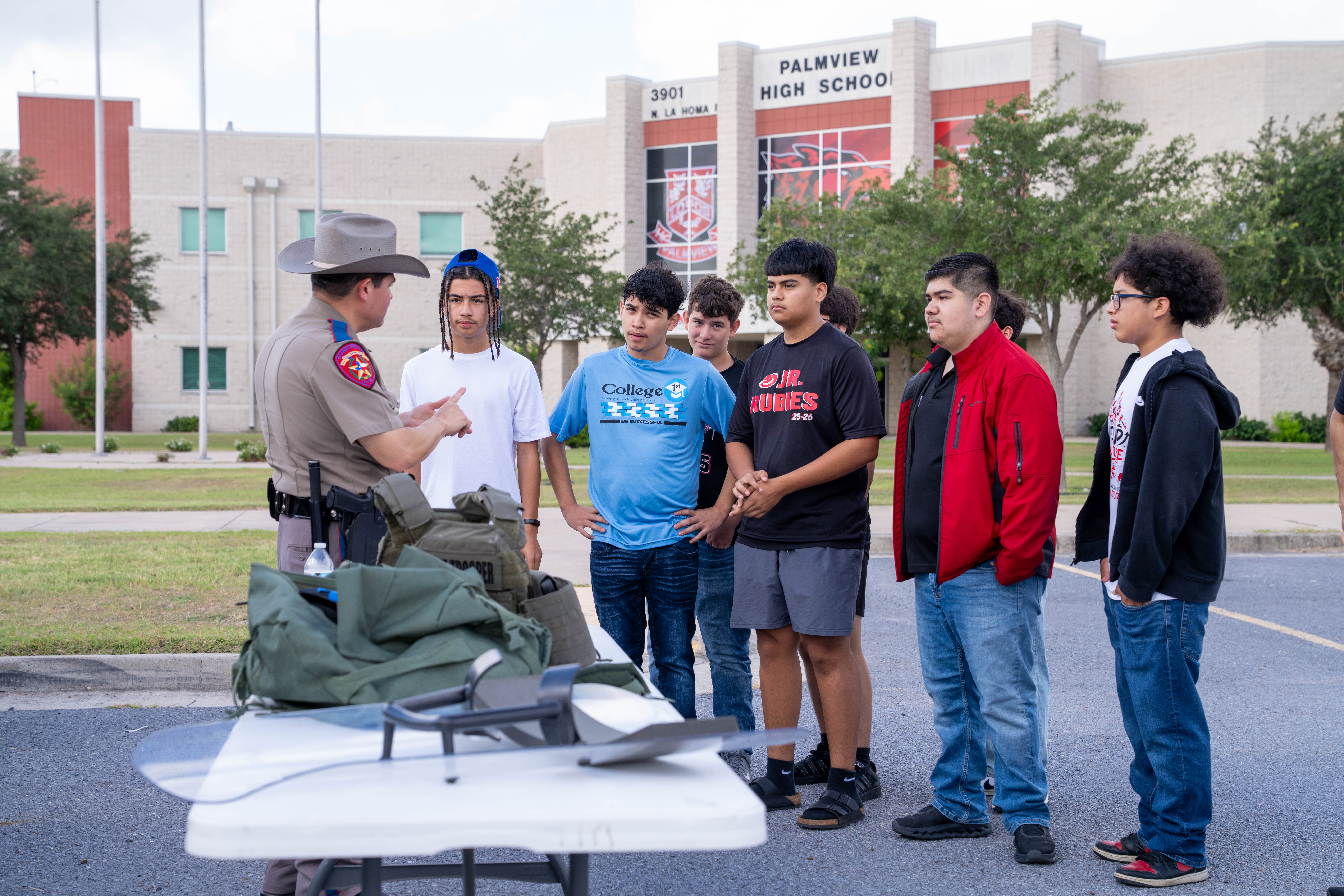 A law enforcement officer in a cowboy hat speaks to a group of high school students outside Palmview High School.