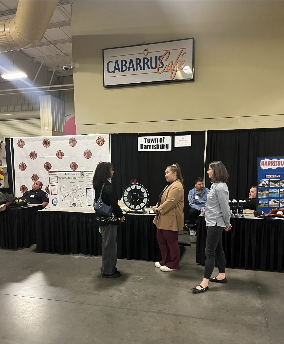People interact at booths at a career fair, with a "Town of Harrisburg" sign visible.