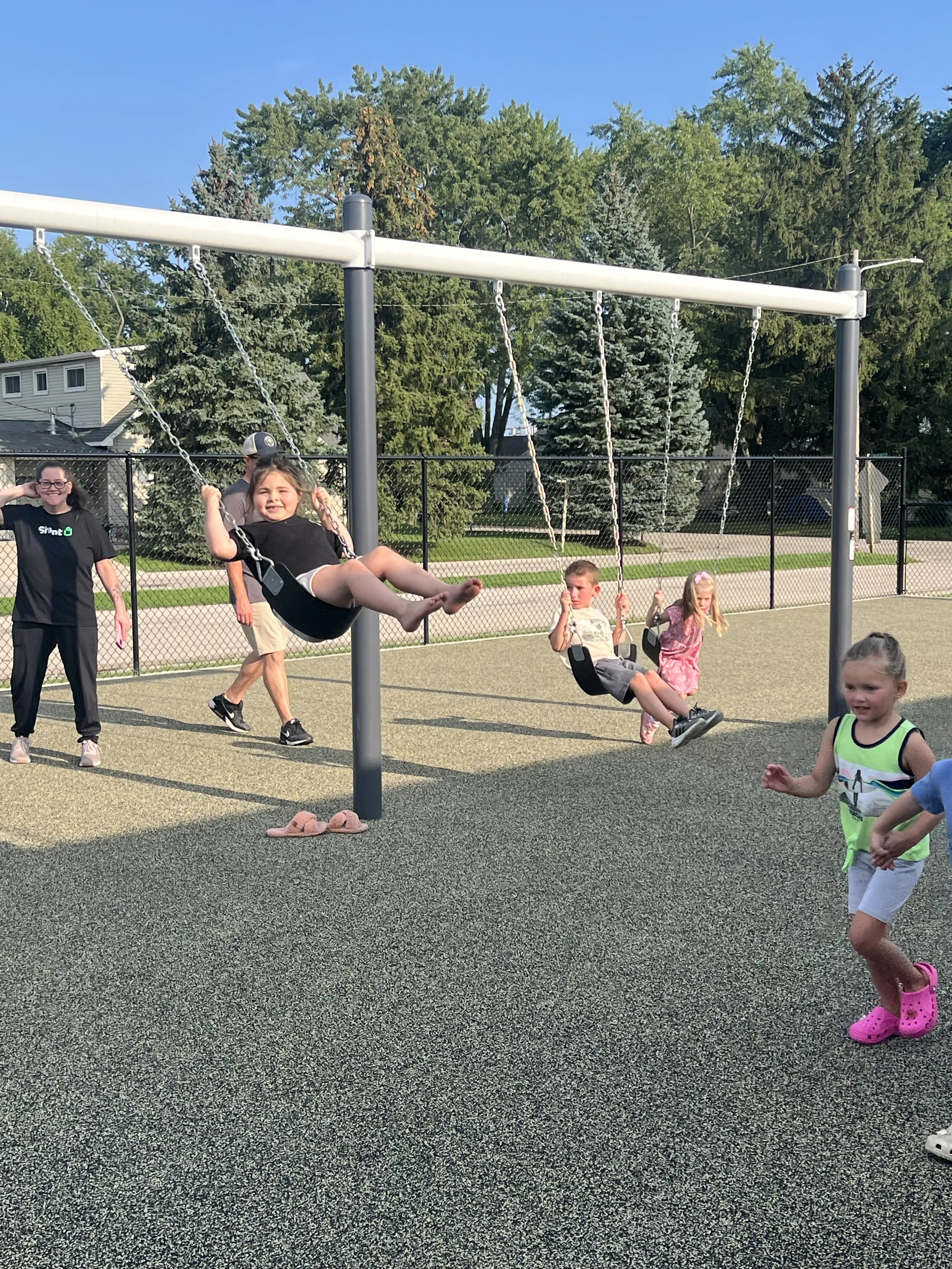 Children laugh and play on swings at a playground on a sunny day.