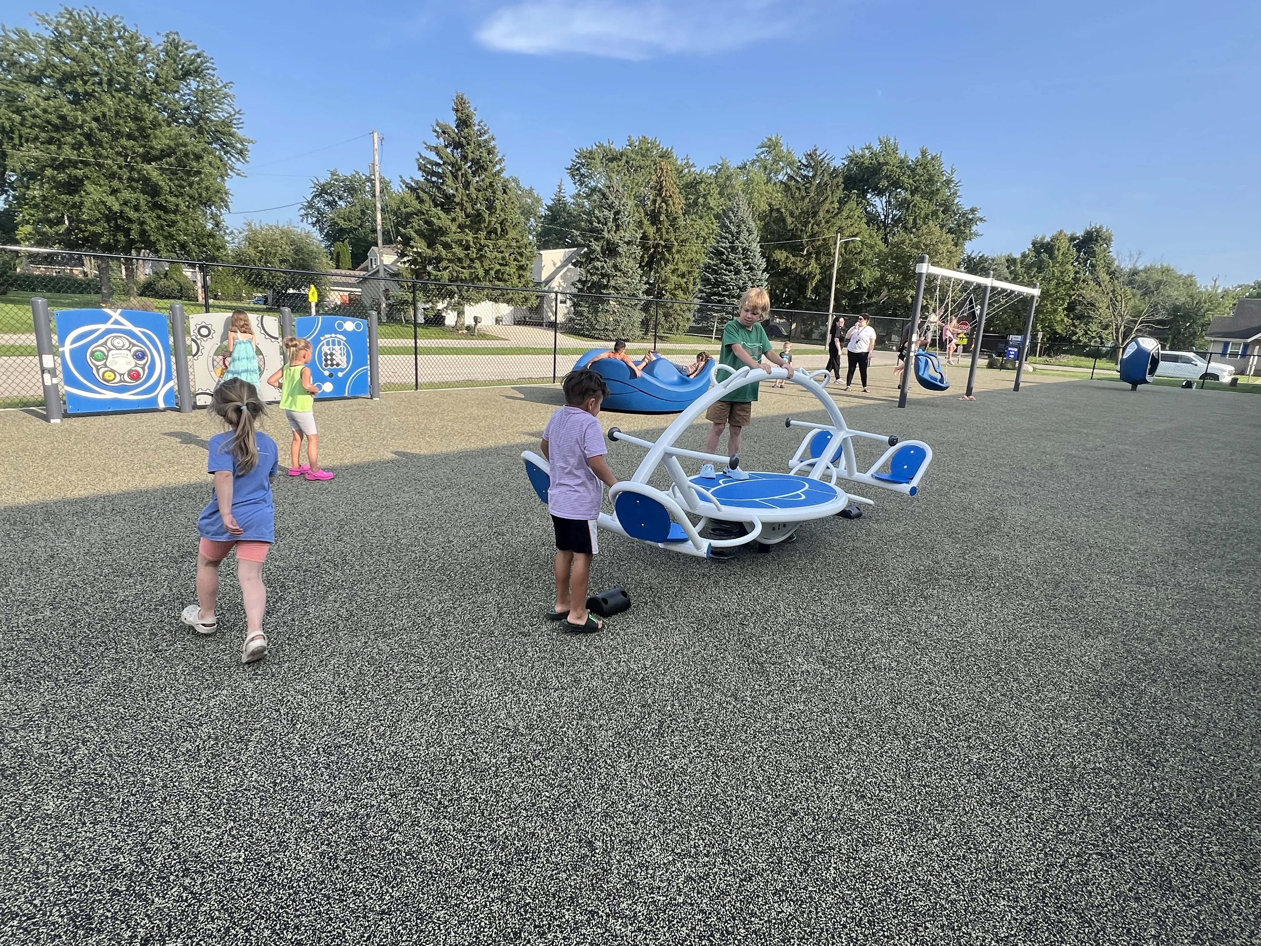Children play on a modern playground with swings, a spinner, and interactive panels.