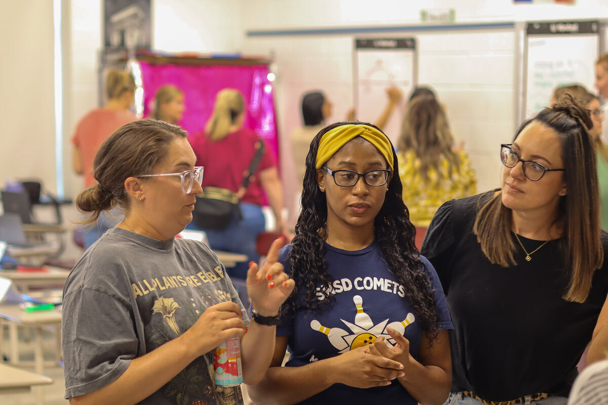 Three women in a classroom setting, engaged in conversation.
