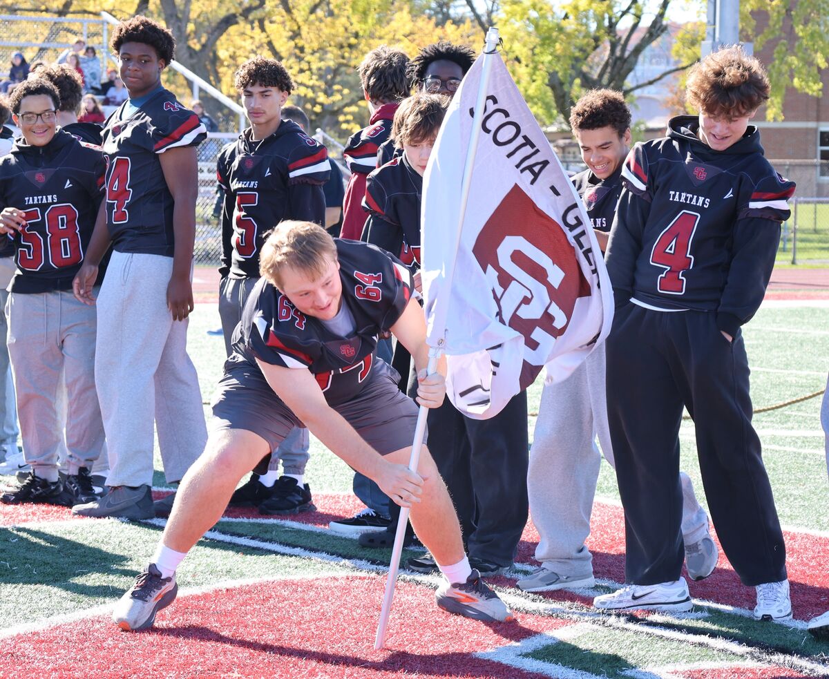 A high school football player plants a white and maroon flag reading "Scotia-Glenville" on the field.
