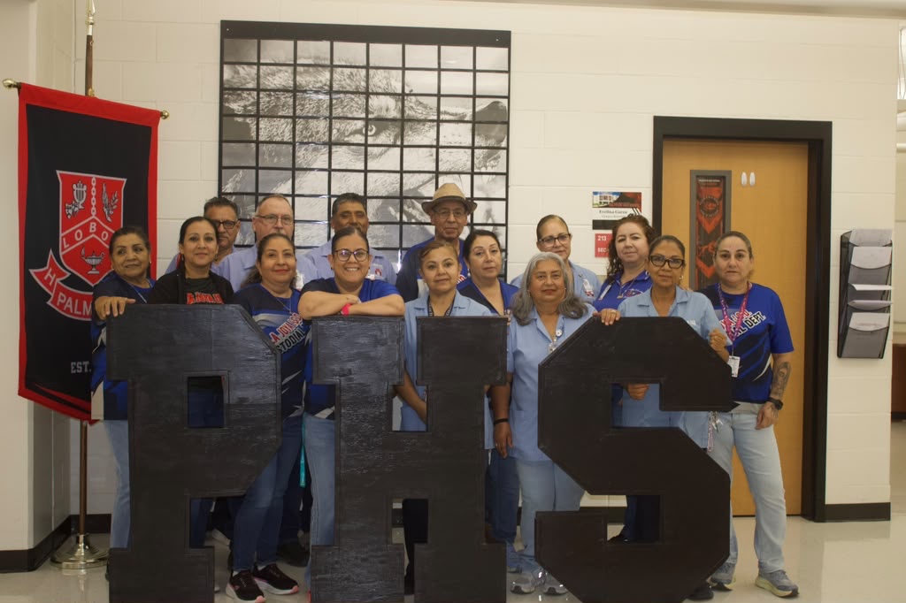 A group of school staff members smiling while holding large black letters that spell PHS inside a building.