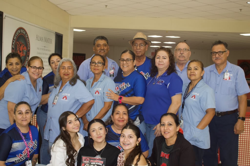 A group of school staff and students pose together indoors, smiling for a group photo.