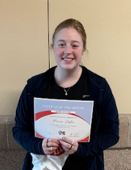 A smiling young woman holds a "Student of the Month" certificate.