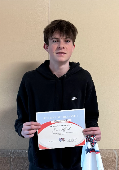 A young man in a black hoodie proudly holds a "Student of the Month" certificate.